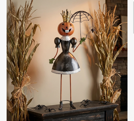 Decorative Halloween figure with a pumpkin head on a wooden surface with dried corn stalks.