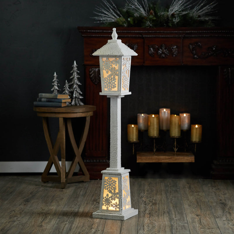 Decorative lantern with warm glow in a room setting with candles and a fireplace.