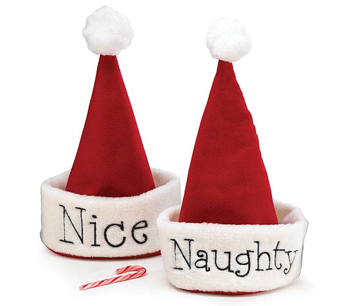 Two plush Santa hat slippers on a white background, one with 'Nice' and one with 'Naughty' embroidered on the white cuff, with a small candy cane in front.