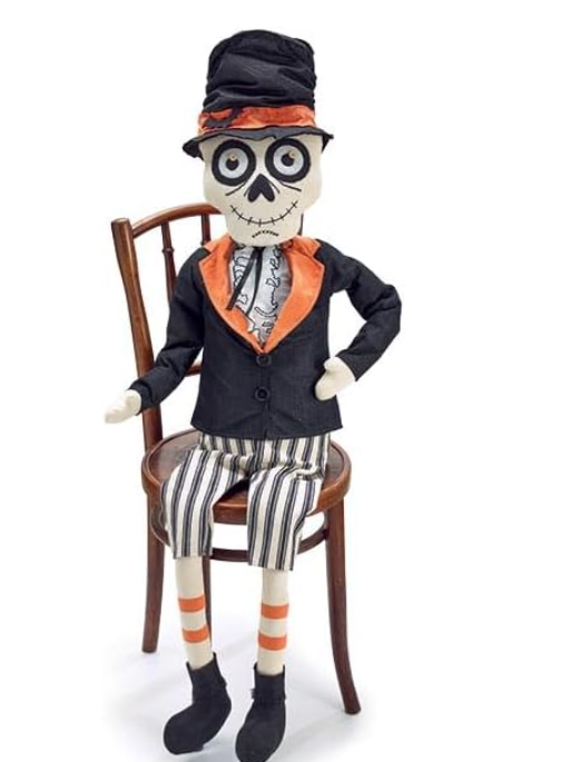 Skeleton doll in formal attire sitting on a chair against a white background