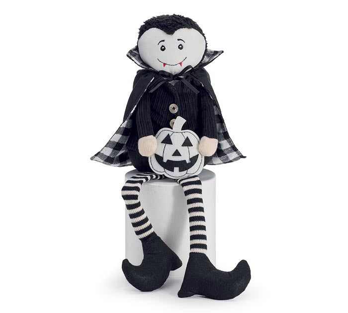A Halloween vampire plush doll with a black cape, striped legs, and a jack-o'-lantern pumpkin, sitting on a white cylindrical pedestal against a white background.