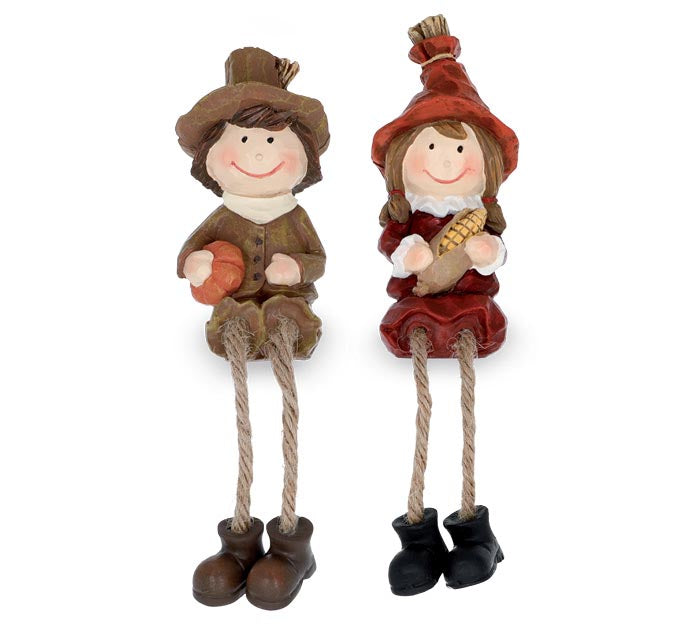 A pair of autumn-themed hanging decorative figurines shaped like a boy and a girl dressed in rustic harvest clothing, seated on rope legs with boots, on a plain white background.