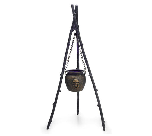 Halloween decoration featuring a black metal cauldron with a skull detail hanging from chains on a tripod stand made of black branches.