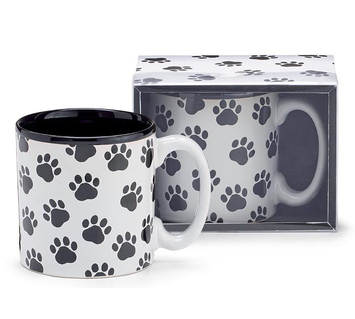 A white ceramic mug with a black interior and black paw print pattern, shown alongside its clear plastic gift box on a white background.