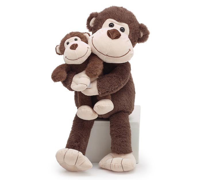 A plush stuffed monkey sitting on a white block against a plain white background. The larger monkey is dark brown with cream-colored face, hands, and feet, while a smaller matching monkey sits in its lap.