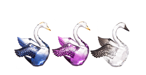 Three glass swan figurines in blue, purple, and clear on a white background