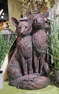 Two resin fox statues on a stand with a decorative background