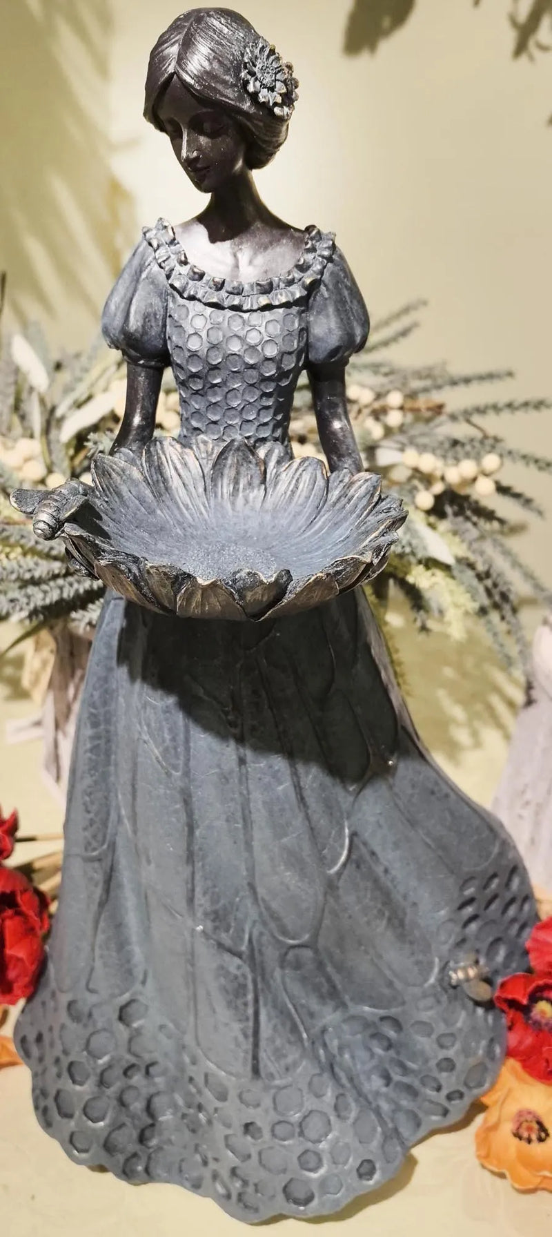 Decorative statue of a woman in a dress with a floral arrangement on a neutral background