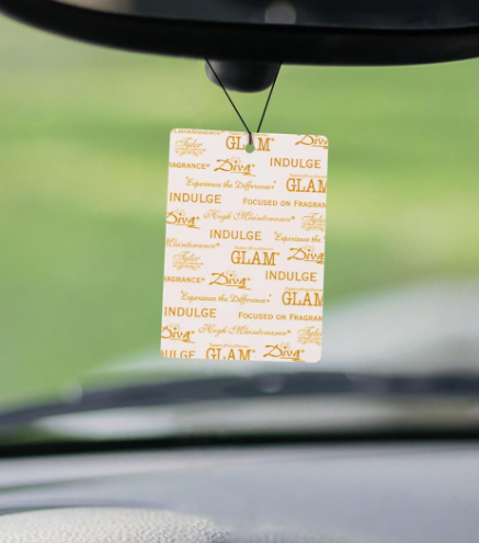 Car air freshener hanging from a hook on a car's dashboard with a blurred green background.