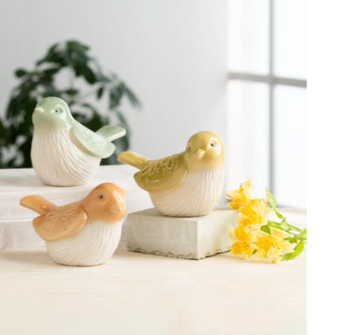 Three ceramic bird figurines on a white surface with a blurred background