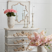 Decorative chest of drawers with floral arrangements and a mirror in a room.