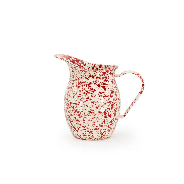 A small enamel pitcher with a red speckled pattern on a white background, featuring a curved handle and a short spout.