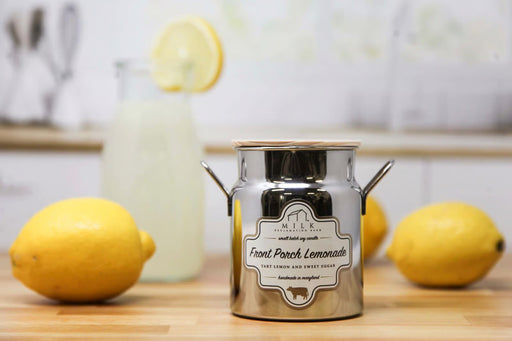 Silver milk churn with lemonade label surrounded by lemons on a wooden surface