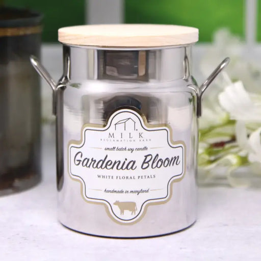 Candle jar labeled 'Gardenia Bloom' by Milk with a wooden lid on a white surface.