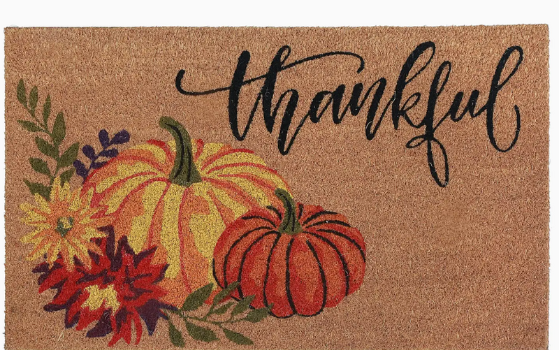 Doormat with pumpkins, flowers, and 'thankful' text on a brown background