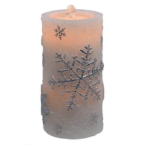 A frosted pillar candle with a warm orange glow from within and raised silver snowflake designs on a white background.
