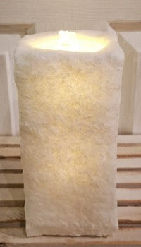 A textured, fluffy white candle-shaped lamp or decorative light glowing with a warm yellow light, set against a neutral indoor background.
