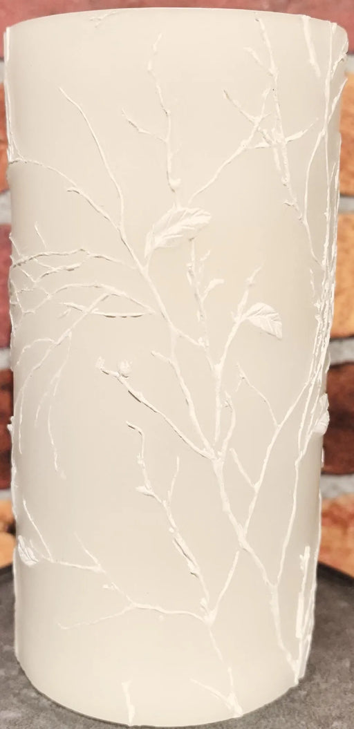 White cylindrical candle with leaf pattern on a wooden surface