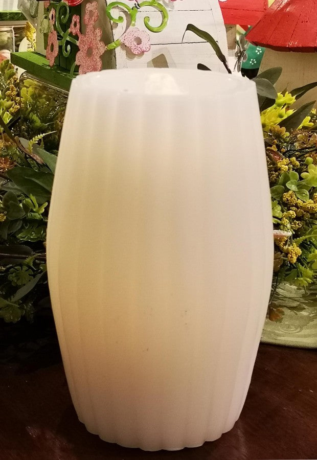 White candle on a wooden surface with greenery in the background