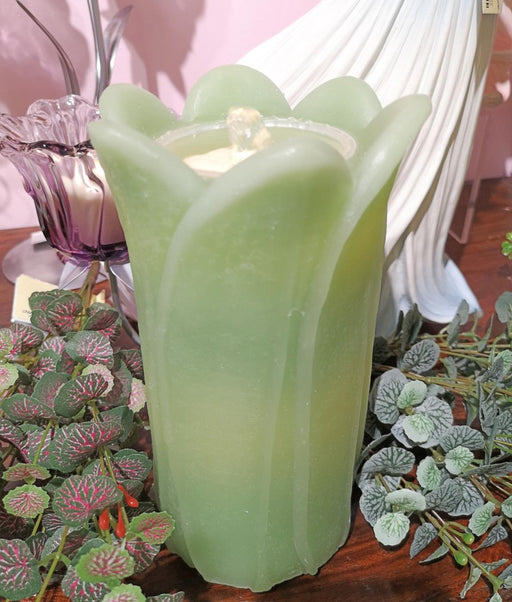 Green candle in a tulip-shaped holder with plants in the background