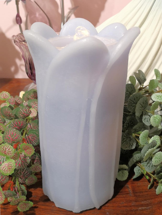 White tulip-shaped candle on a wooden surface with green plants in the background