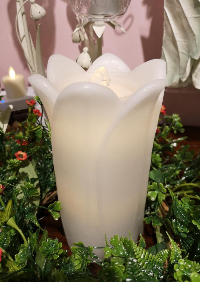 White floral-shaped candle holder with a candle inside, surrounded by greenery.