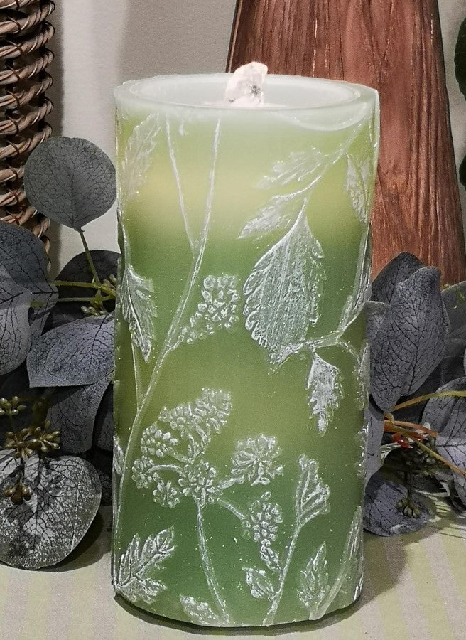Green candle with leaf pattern on a surface with decorative elements