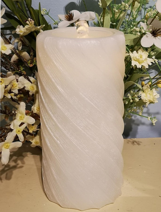 Decorative white candle with wavy texture on a surface with flowers in the background