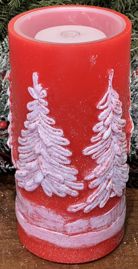 Red candle with white tree designs on a wooden surface