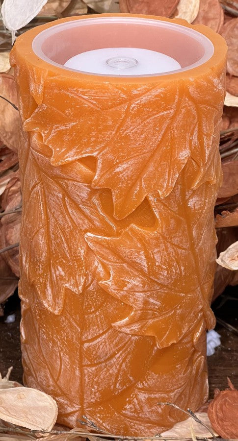 Decorative candle with leaf pattern on a wooden surface
