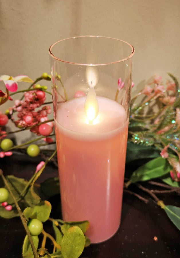 Pink candle in a glass holder with floral decorations on a dark surface