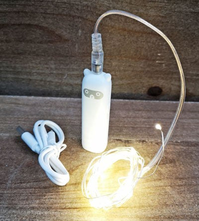 White bottle with LED string light on a wooden surface