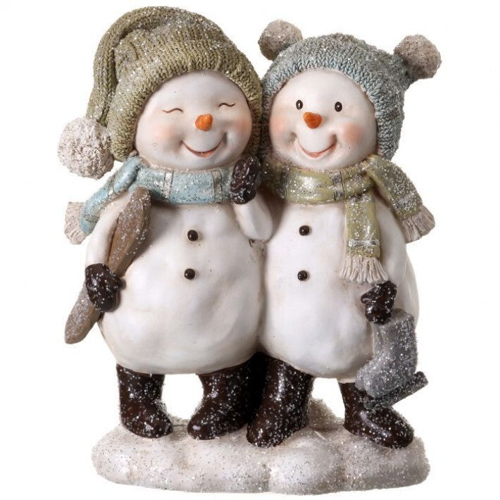 A pair of decorative snowman figurines standing side by side on a glittery base. One snowman wears an olive green knit hat and scarf, while the other wears a gray knit hat and scarf.