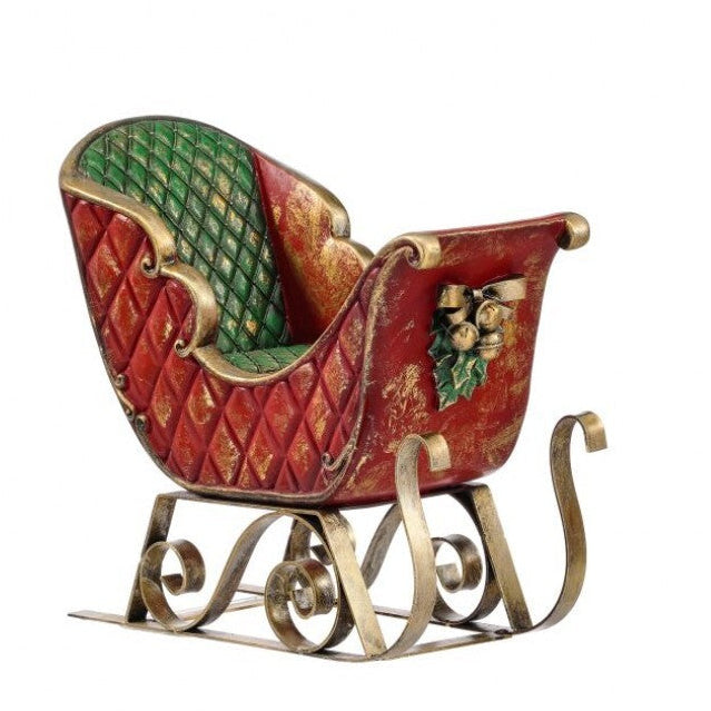 A decorative Christmas sleigh figurine with a distressed red body, green quilted interior, gold-toned scroll metal base, and a small holly and gold ornament accent on the side, shown on a plain white background.