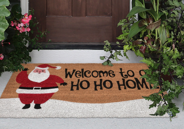 Doormat with Santa Claus design and 'Welcome to a Ho Ho Home' text on a door entrance.