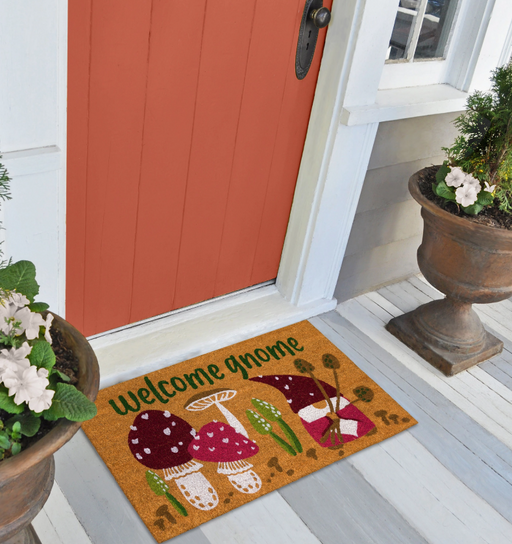 Doormat with mushroom design and 'Welcome Gnome' text on a wooden floor in front of a red door.