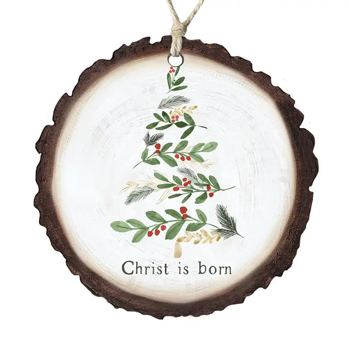 A round Christmas ornament shaped like a natural wood slice, featuring a painted green holly tree with red berries and the text 'Christ is born' on a white background.
