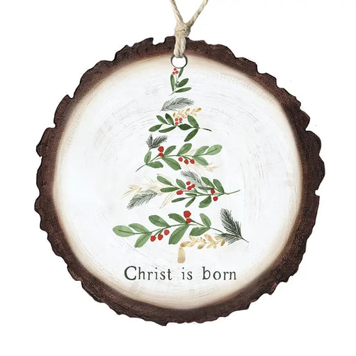 A round Christmas ornament shaped like a natural wood slice, featuring a painted green holly tree with red berries and the text 'Christ is born' on a white background.