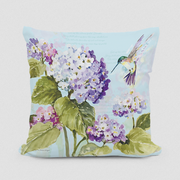 A square decorative pillow with an image of a hummingbird and hydrangea flowers in blue, green, and purple colors.