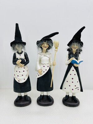 Three witch figurines with black hats and dresses on a white background