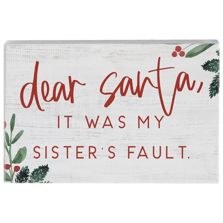 A rectangular white wooden sign with a rustic finish, featuring the text 'dear santa, it was my sister's fault.' in red lettering, decorated with watercolor green holly leaves and red berries in the corners.