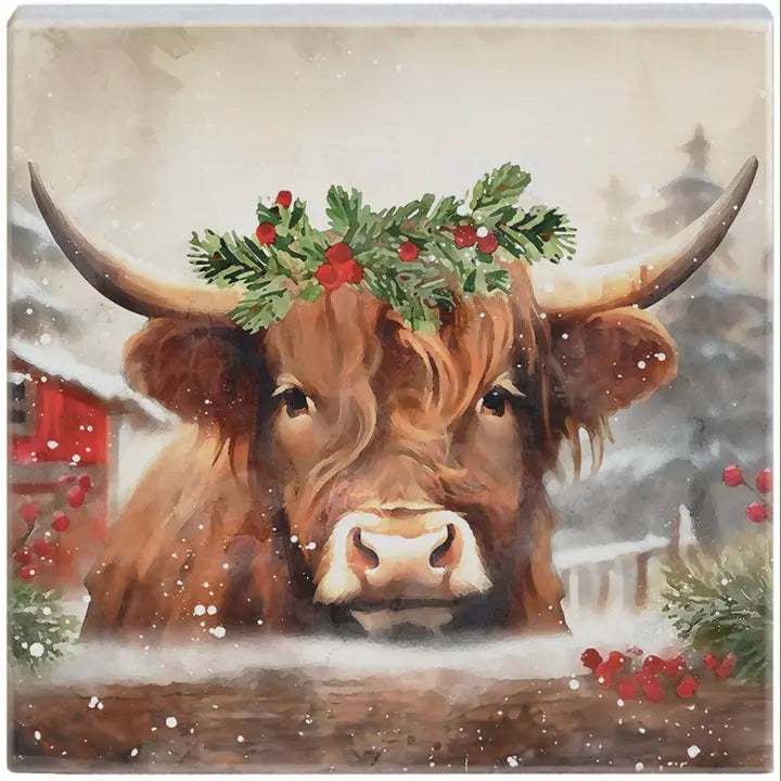 A square decorative artwork featuring a festive watercolor illustration of a brown Highland cow with long horns, wearing a green holly wreath with red berries. The background depicts a snowy, softly blurred winter scene with a red barn and distant house.