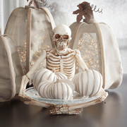 Decorative skeleton figure sitting on pumpkins inside a glass dome with LED lights.