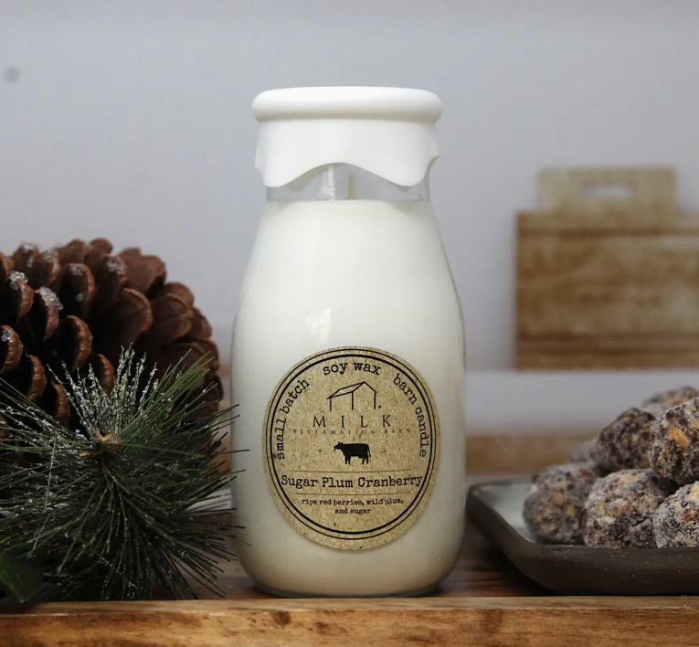 Bottle of soy wax candle with a label on a wooden surface with decorative items.