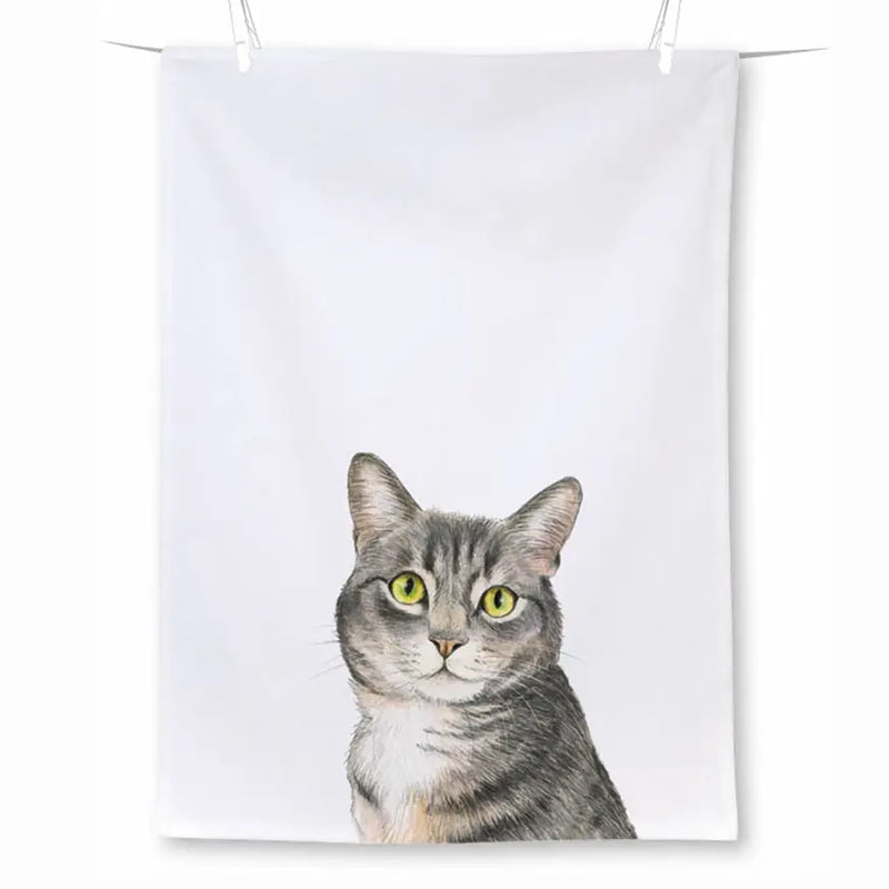 A white fabric tea towel with a printed illustration of a gray tabby cat with bright yellow-green eyes, shown hanging against a white background.