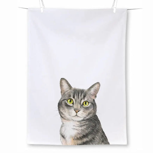 A white fabric tea towel with a printed illustration of a gray tabby cat with bright yellow-green eyes, shown hanging against a white background.
