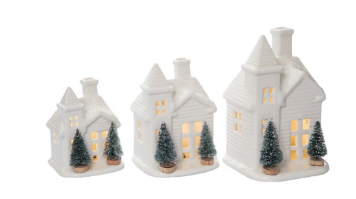 Set of three white ceramic houses with lit interiors and small trees on a white background