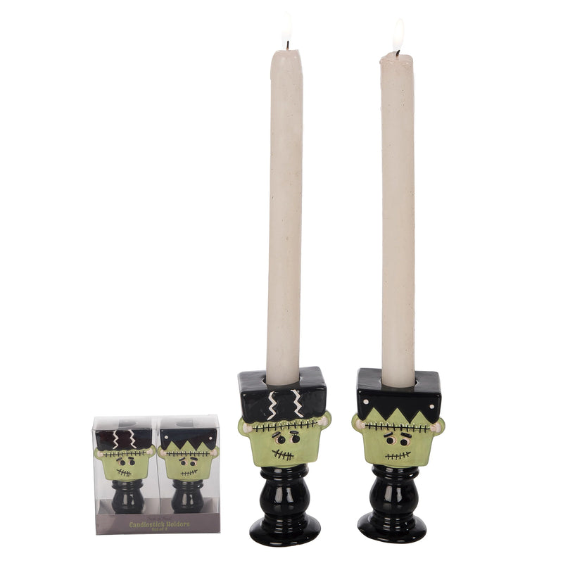 Two black candle holders with green faces and white candles on a white background