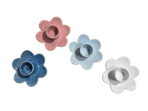 Four flower-shaped candle holders in pink, blue, white, and gray on a white background.
