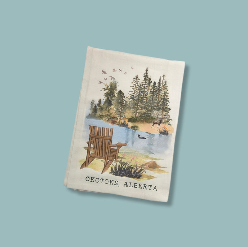 Tea towel with a scenic design of a lake and trees, featuring 'Okotoks, Alberta'.